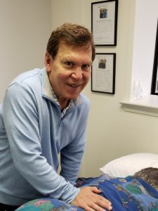 Tom looks up and smiles while working on lower back of patient